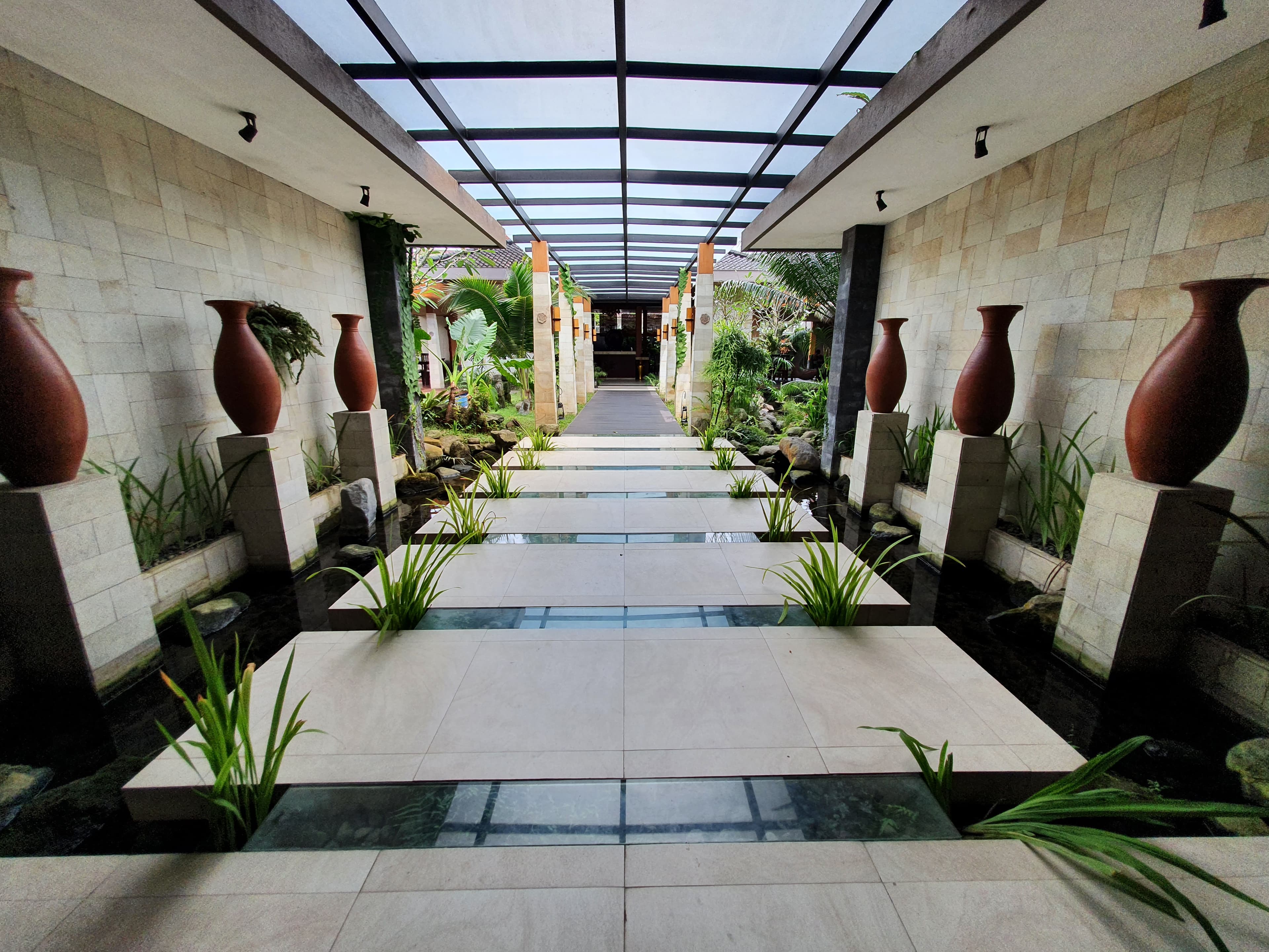 Walkway taman dengan deretan vas keramik dan tanaman tropis